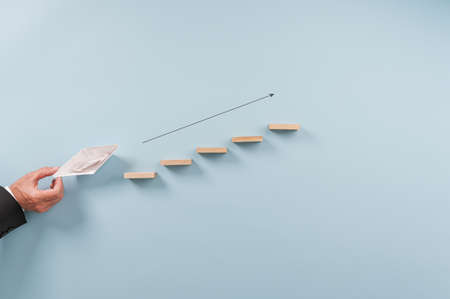 Conceptual image of business vision and leadership - origami made paper boat sailing upwards the steps towards success. Over blue background.の写真素材