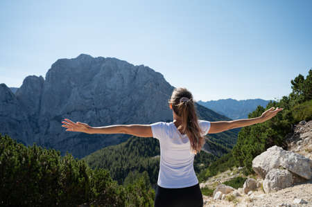 View from behind of a young woman standing outside in highland with her arms spread widely enjoying peace and freedom.の写真素材