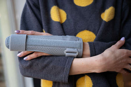 Closeup view of a woman cradling her injured arm with a brace on her middle finger.