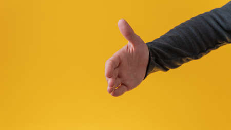 Male hand offering a handshake over yellow background.の写真素材