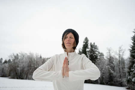 Young woman meditating with her palms joined infront of her chest standing outside in snowy winter nature.の写真素材