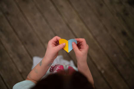 Top view of a child holding heart shaped paper in the colors of ukrainian flag - blue and yellow -  in a conceptual image of ukrainian orphans.の写真素材
