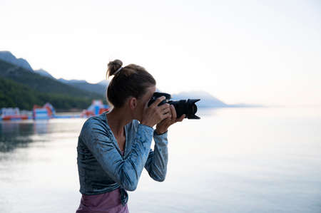 Young female photographer taking photos by thea sea in the early summer morning.