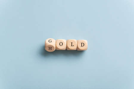 Conceptual image of global gold market - word gold spelled on wooden dice turning into hold. Over blue background.の写真素材