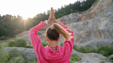 View from behind of a young woman practicing mindfulness with her palms joined above her head...