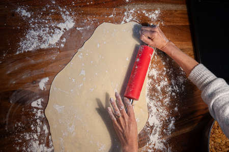 Overhead view of female hands rolling homemade pastry dough with a rolling pin on domestic dining table.の写真素材