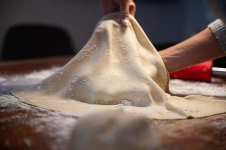 Low angle closeup view of a woman stretching and pulling homemade vegan pastry dough for strudel or pie.の写真素材