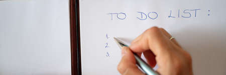 Wide view image of female hand writing a To do list on white sheet of paper. Overhead view.