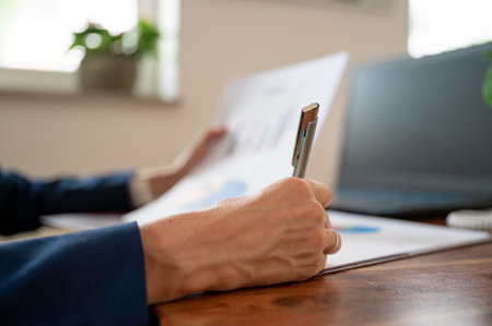 Low angle closeup view of hand of a businesswoman signing a document or report working at her office desk.の写真素材