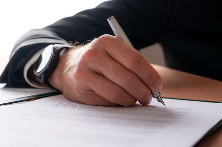 Low angle closeup view of a hand of a businessman with elegant watch on his wrist, signing a...