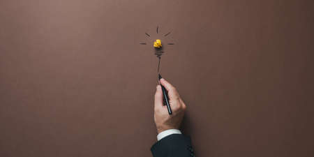 Hand of a businessman drawing a light bulb made of yellow wrinkled paper over brown backround....