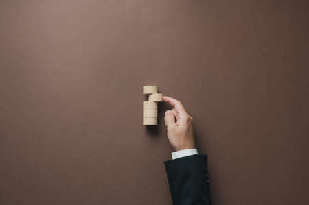 Hand of a businessman pushing a blank wooden cut circle into a stack of them  in a conceptual image. Top view over brown background.の写真素材