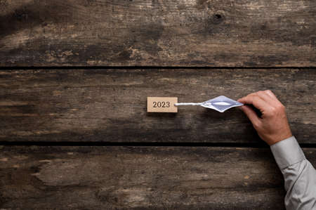 Male caucasian hand pulling an origami paper boat with a wooden peg with 2023 sign on it attached to...