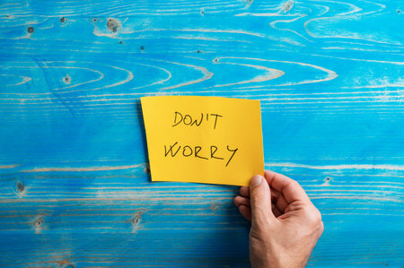 Male hand placing a bright yellow paper with Dont worry sign over textured aged blue wooden background.の写真素材