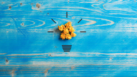 Light bulb made of smashed yellow papers and hand drawn glow placed over aged blue textured wooden background.の写真素材
