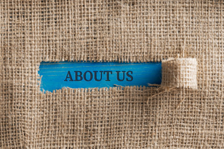 Top view of a rough linen fabric with a torn window in the middle with an About us  sign written in it on a blue surface.の写真素材