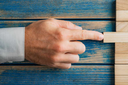 Hand of caucasian businessman pushing a wooden peg into a stack of them in a conceptual image of building a business and startup.の写真素材
