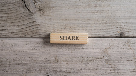 Wooden peg with Share sign on it placed over textured light colored wooden backgorund.