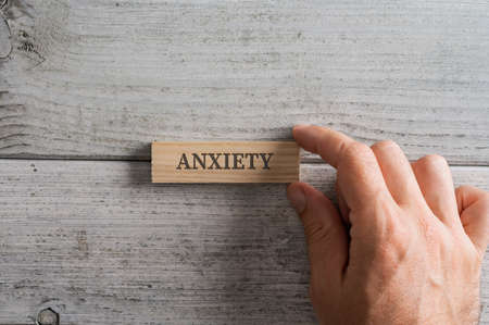 Male hand placing wooden peg with the word Anxiety on it over textured white wooden background.の写真素材