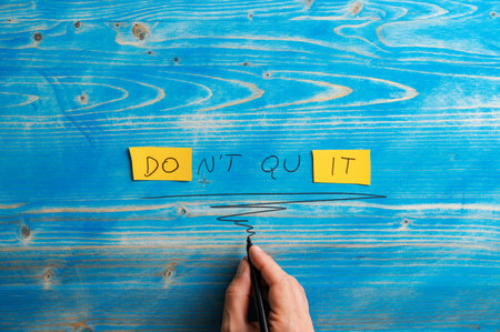 Male hand writing a Dont quit, Do it sign on bright yellow papers over aged blue wooden background.の写真素材