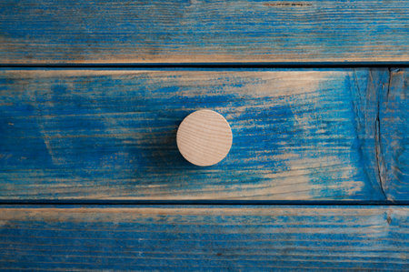 Blank wooden cut circle placed over blue textured wooden background.