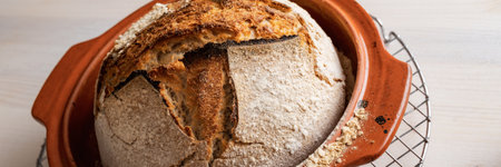 Wide view image of delicious crusty homemade sourdough bread cooling of in clay pot.の写真素材