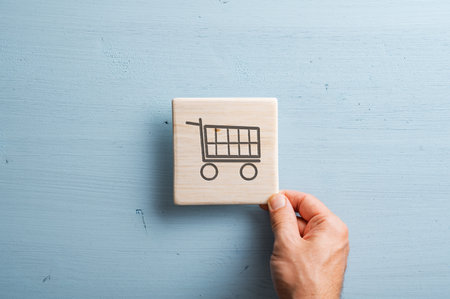 Male hand holding wooden tile with a shopping cart icon on it. Over pastel blue wooden background.の写真素材