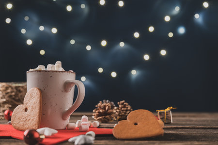 Christmas holiday still life with cup of delicious hot chocolate topped with marshmallows placed on rustic wooden desk with seasonal decorations and large heart shaped cookies.の写真素材
