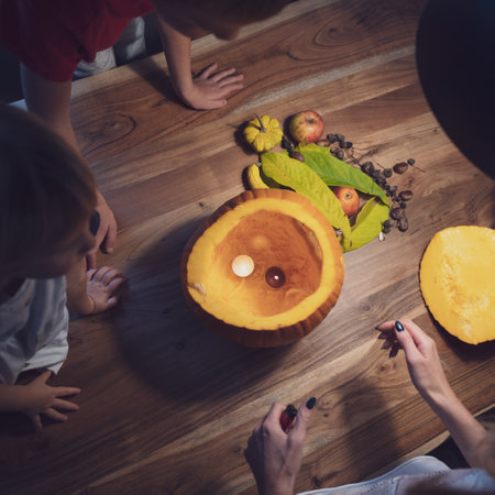 Overhead view of a mother and her children preparing halloween decoration with pumpkin and autumn fruits on a domestic dining table.の写真素材