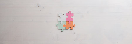 Wide view image if four blank puzzle pieces of various pastel colours joined together over wooden background.の写真素材