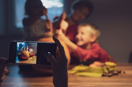 Mother using her mobile phone to take photos of her excited three kids with a halloween pumpkin they had carved.の写真素材