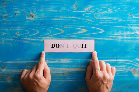 Male hands holding a paper with Dont quit sign fading into a Do it sign written on it, placing it on textured blue background.の写真素材