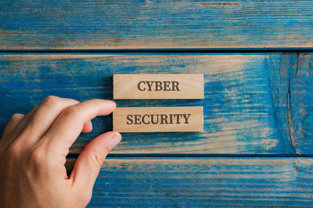 Male hand assembling a Cyber security sign written on two wooden pegs placed over textured blue wooden background.の写真素材