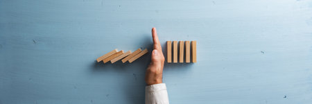 Hand of a businessman stopping collapsing dominos to prevent a disaster and crisis. Top view of blue wooden background.の写真素材