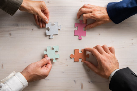 Four business people holding matching puzzle pieces of various pastel colours in a conceptual image of business teamwork and cooperation.の写真素材