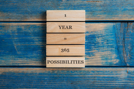 One year is 365 possibilities sign written on a stack of wooden pegs placed over blue wooden...