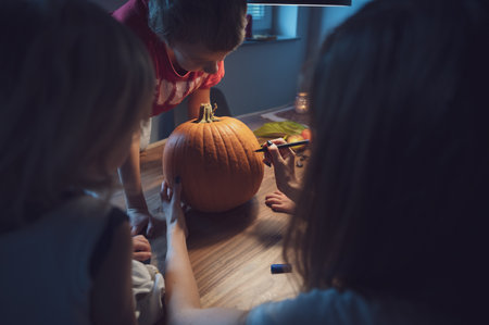 Mother and her three children drawing on a pumpkin to carve it for halloween holidays.の写真素材