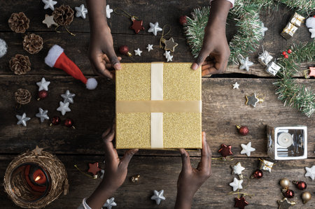 Two black coloured girls holding a shiny golden gift box placed on a festive decorated wooden table...