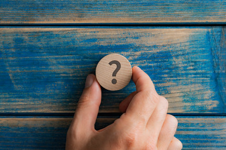 Male hand placing a wooden cut circle with a question mark on it over an aged blue background.の写真素材