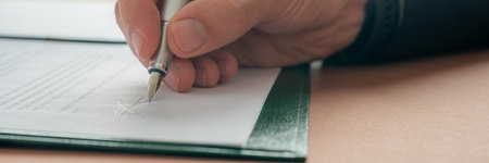 Low angle closeup view of casucasian male hand signing a document or contract with an ink pen. Wide view image.の写真素材