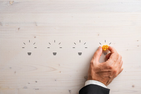 Silhouettes of four light bulb shapes carved into wooden background with a hand of a businessman placing smashed yellow paper in the fourth one. Conceptual image of idea and innovation.の写真素材