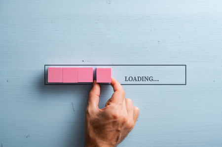 Male hand placing a pink wooden blocks into a loading bar with a Loading sign. Over pastel blue wooden background.の写真素材