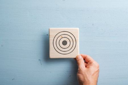 Male hand placing a wooden tile with a target symbol drawn on it over a pastel blue wooden background.の写真素材