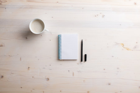 Blank spiral notebook and open black spiral pen placed on simple wooden desk with a cup of fresh coffee.の写真素材