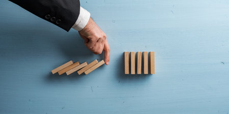 Hand of a businessman interrupting collapsing dominos with his finger in a conceptual image of...