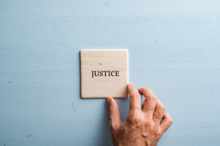 Word Justice printed on wooden tile placed over pastel blue background.の写真素材