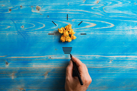 Light bulb made of smashed yellow papers and male hand drawing its base in a conceptual image of energy and innovation. Over textured blue wooden background.の写真素材