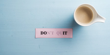 Dont quit sign with vanishing letters to spell a Do it sign on pink paper placed next to a cup of coffee on pastel blue wooden background.の写真素材