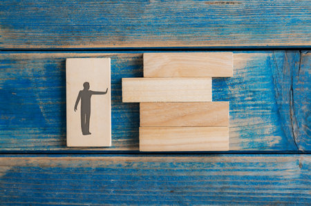 Silhouette of a man with a stop gesture pushing a wooden peg into a stack of them in a conceptual image of building a new business or opportunity.の写真素材