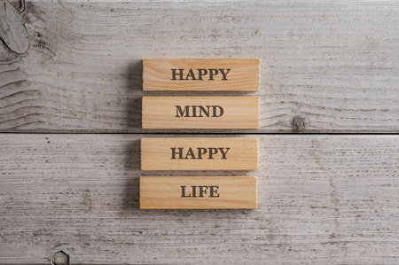 Happy mind happy life sign written on a stack of wooden pegs placed over white wooden background.の写真素材